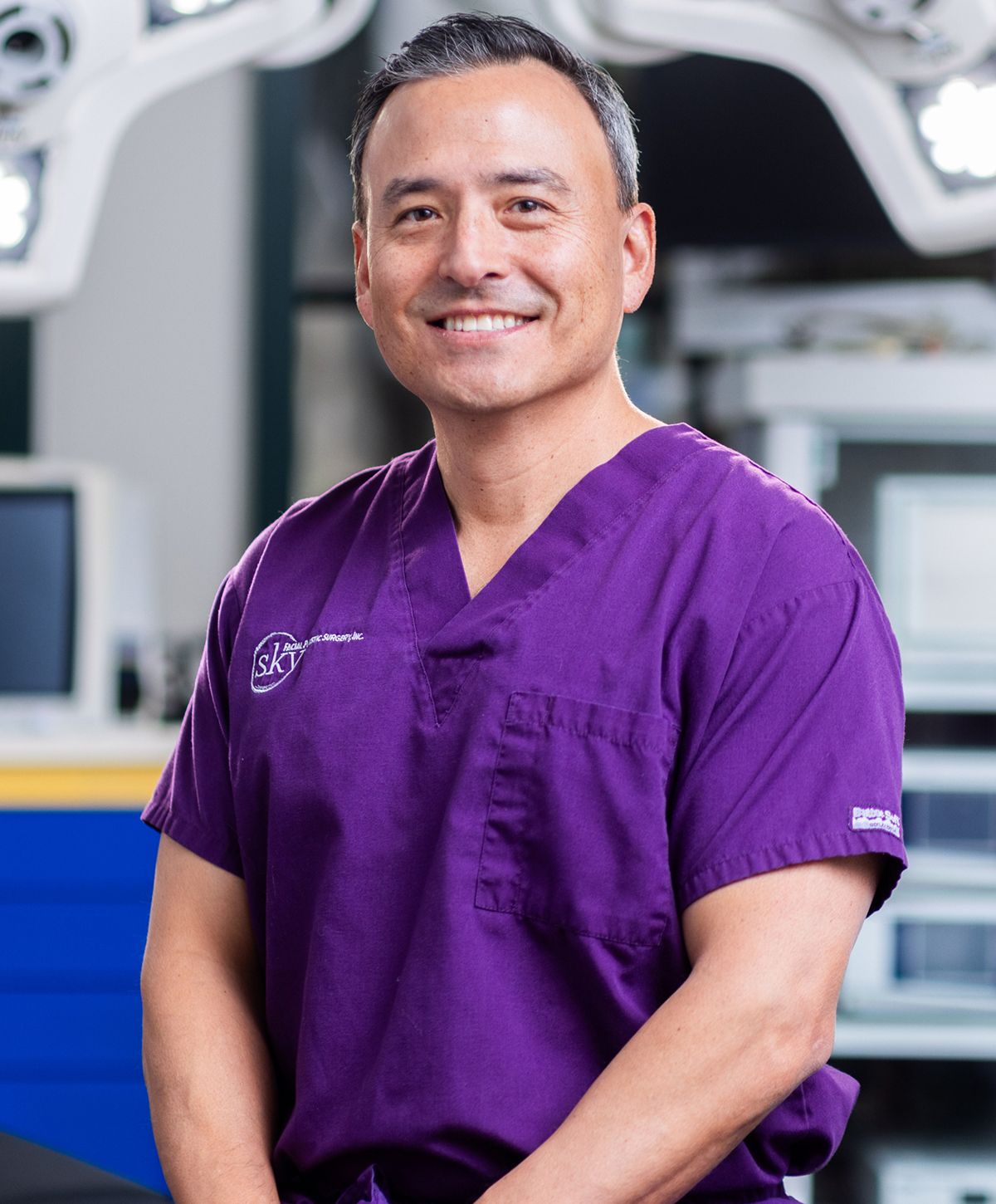 Male doctor smiling in purple scrubs.