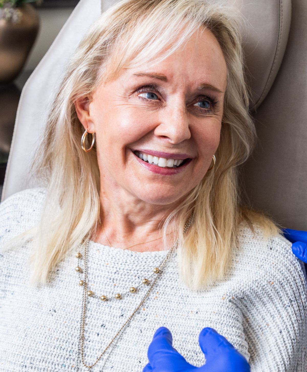 Smiling woman receiving treatment, wearing sweater and jewelry.
