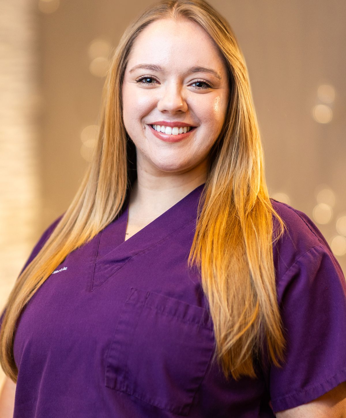 Smiling woman in purple medical scrubs.