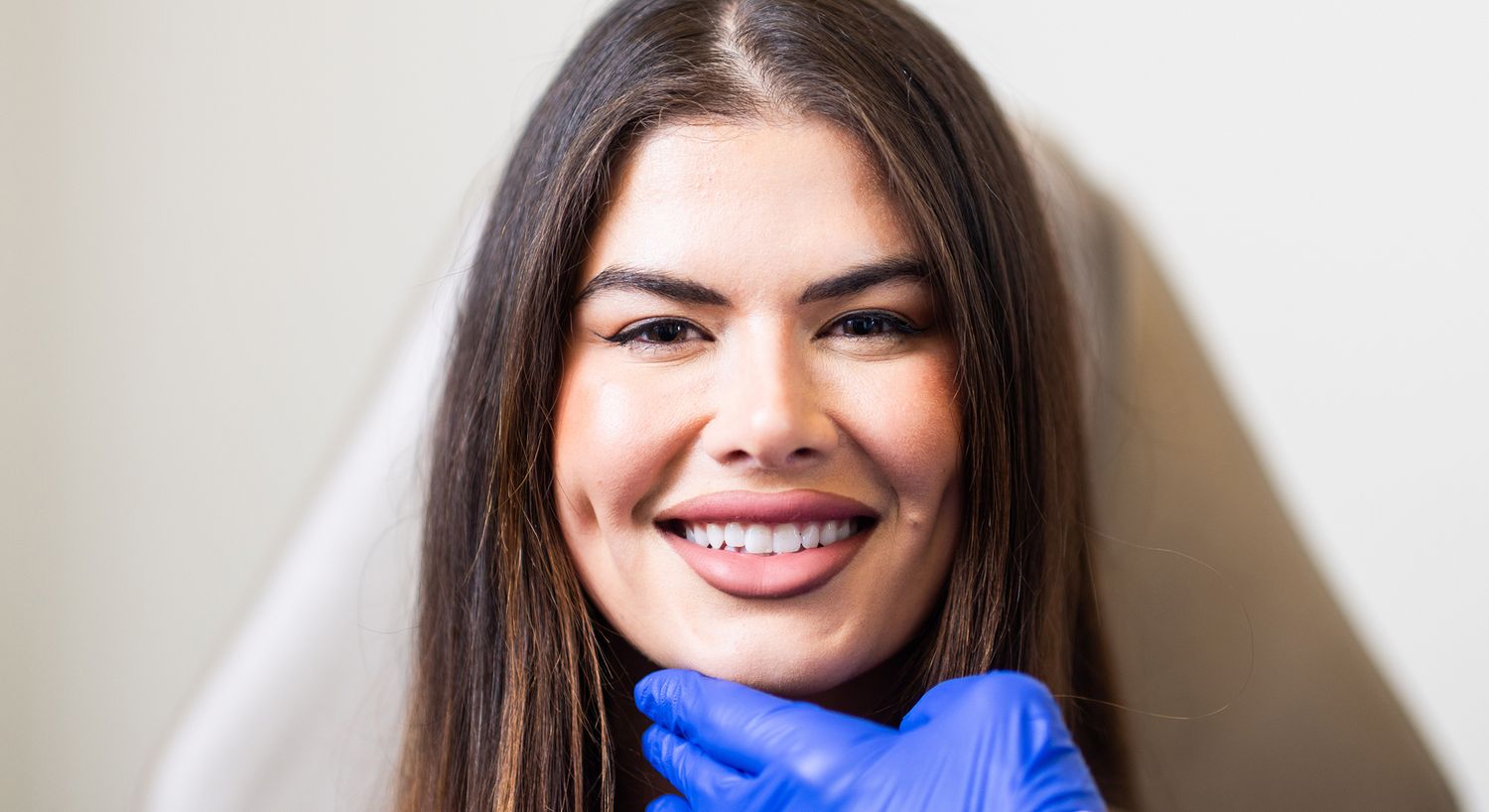 Smiling woman with gloved hand touching chin.
